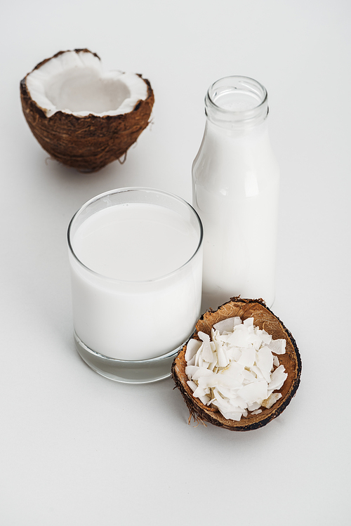 organic vegan coconut milk near coconut half and chips on grey background