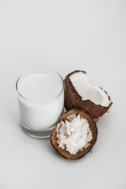 organic vegan coconut milk in glass near coconut half and chips on grey background