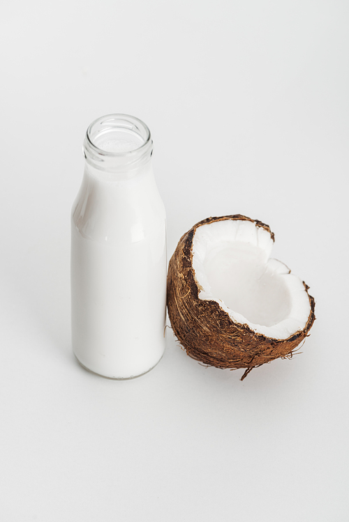 organic vegan coconut milk in bottle near coconut half on grey background