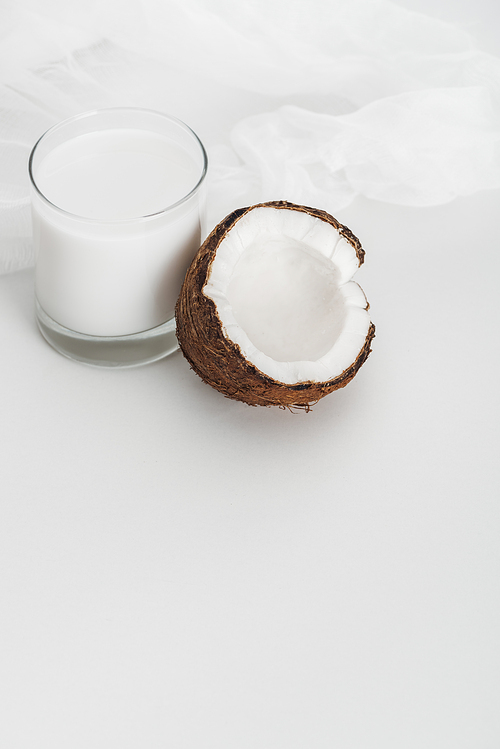 organic vegan coconut milk in glass near coconut half and cheesecloth on grey background