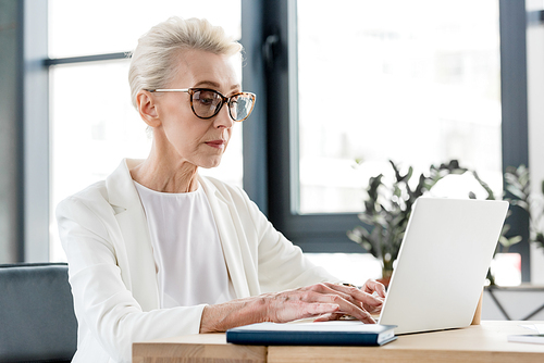 senior businesswoman in eyeglasses using laptop in office
