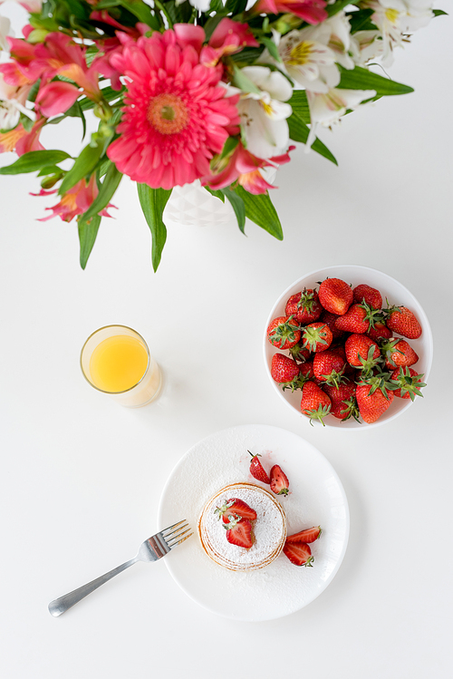 top view of tasty pancakes with strawberries and flowers in vase