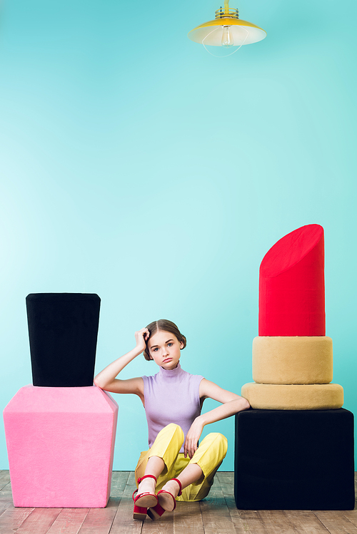 elegant fashionable girl sitting between big nail polish and lipstick on floor