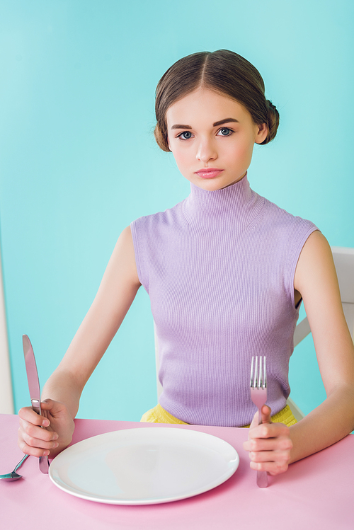 beautiful girl with knife, fork and empty plate sitting at table