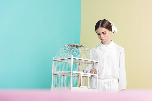 attractive fashionable girl with parrot in white cage