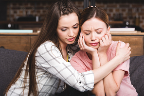 young woman cheering up crying female friend at home