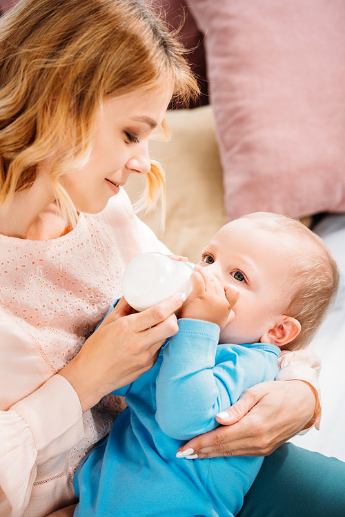 loving mother feeding her little child with baby bottle at home