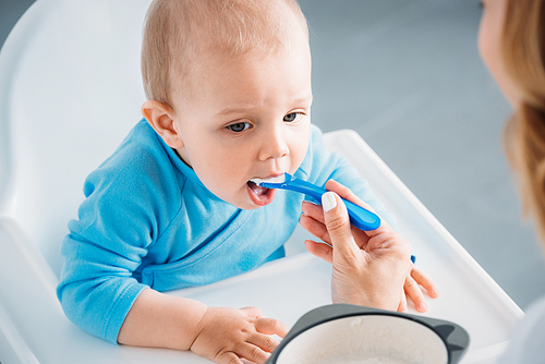 cropped shot of mother feeding adorable child with porridge