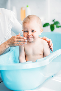 cropped shot of mother washing her little child in plastic baby bathtub at home