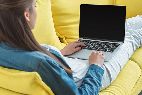 cropped shot of young woman using laptop with blank screen on sofa at home