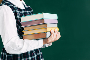 cropped shot of schoolgirl holding pile of books while standing near blackboard