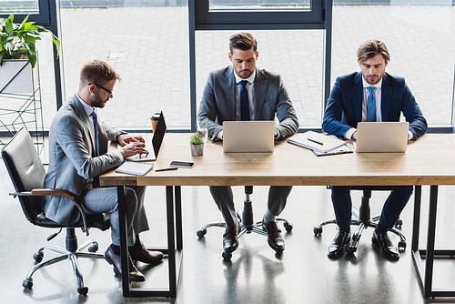 high angle view of focused young businessmen using laptops at workplace