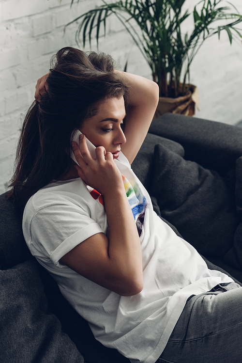 young transgender man talking by phone on couch at home