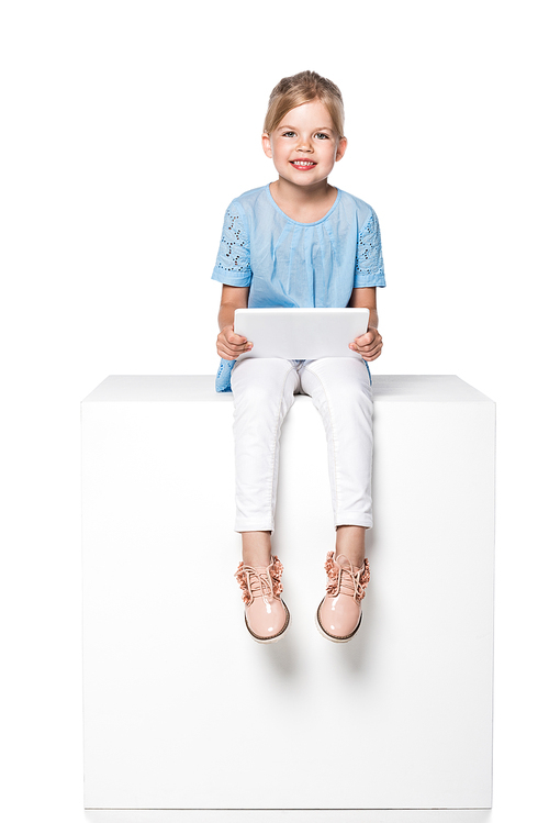 child using digital tablet and sitting on white cube isolated on white