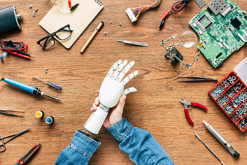 cropped image of man with amputee putting on robotic hand on table with tools