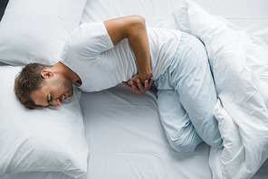 top view of man lying in bed and suffering from stomach pain