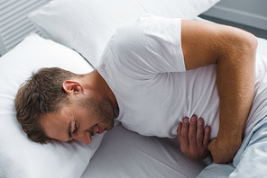 high angle view of man lying in bed and suffering from stomach pain