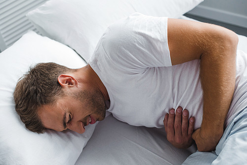 high angle view of man lying in bed and suffering from stomach pain