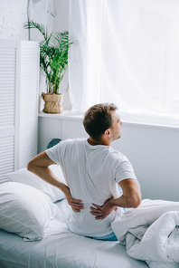 high angle view of man sitting on bed and suffering from back pain