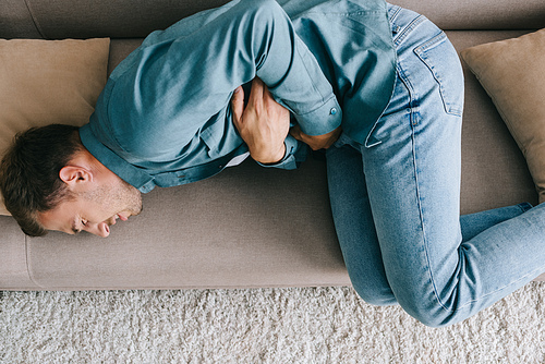 top view of man lying on sofa and suffering from stomach ache