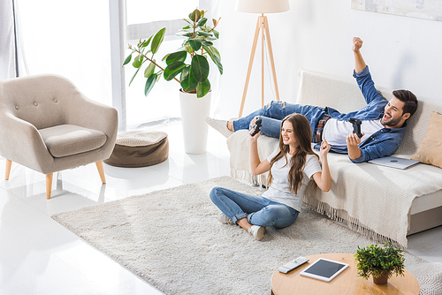 high angle view of happy young couple with joysticks gesturing by hands and celebrating victory in video game at home