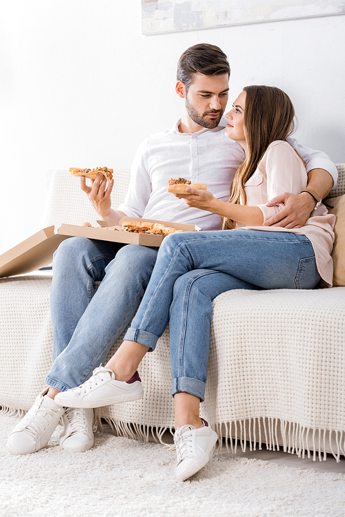 young couple with pizza resting on sofa at home
