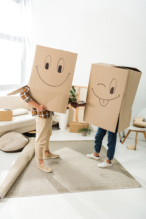 obscured view of couple with cardboard boxes on heads holding hands at new house, moving home concept