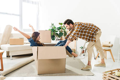 side view of couple having fun with cardboard box at new house, moving home concept