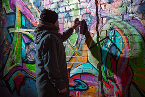 street artist painting graffiti with aerosol paint on wall at night