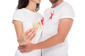 cropped shot of couple with packed condom and aids ribbons on t-shirts isolated on white