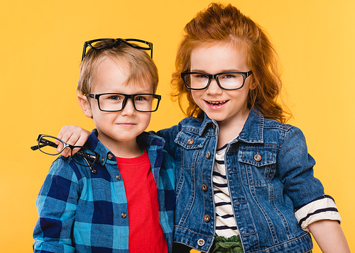 portrait of smiling kids in eyeglasses isolated on yellow