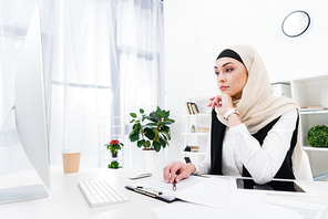 thoughtful businesswoman in hijab sitting at workplace in office