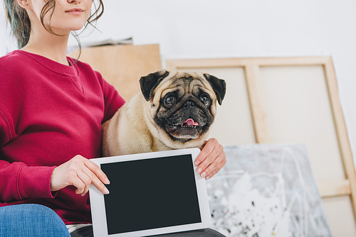 Young woman showing tablet screen and hugging pug dog