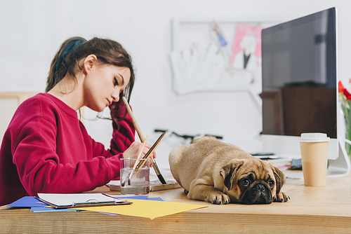 Attractive young girl drawing while pug waiting on her table