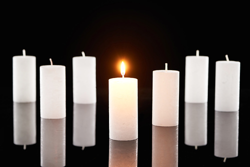 selective focus of burning white candles glowing near another isolated on black
