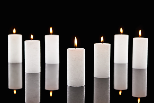 selective focus of burning white candles glowing isolated on black