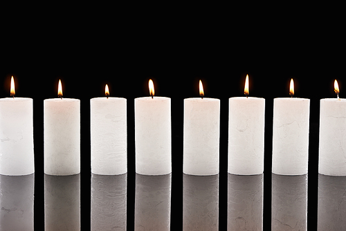 burning white candles glowing in line isolated on black