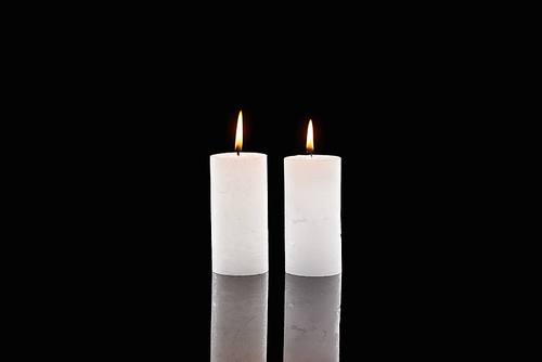 two burning white candles glowing isolated on black
