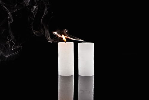 burning and extinct white candles with smoke on black background