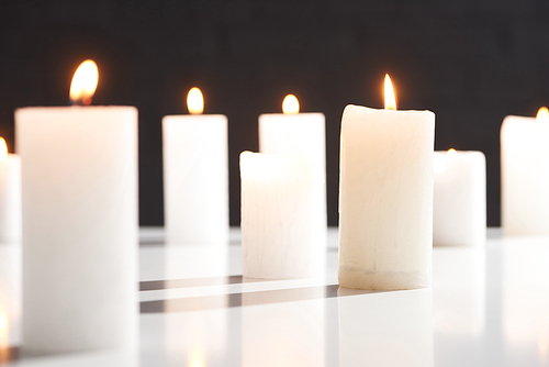selective focus of burning white candles on white surface glowing isolated on black