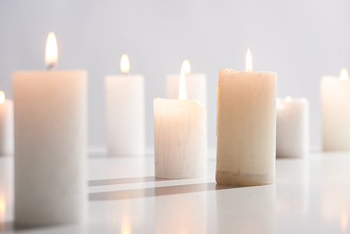 selective focus of burning white candles on white surface glowing isolated on grey