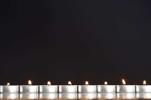 burning candles arranged in line glowing isolated on black