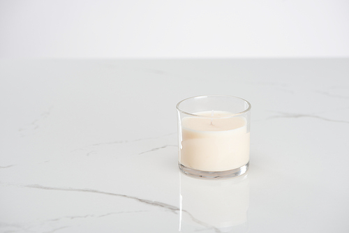 white candle in glass on marble white surface