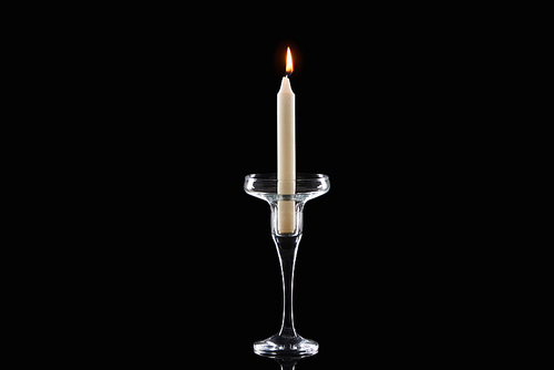 burning white candle glowing in glass candlestick isolated on black