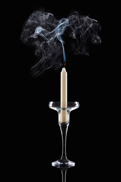 extinct white candle in glass candlestick with smoke on black background