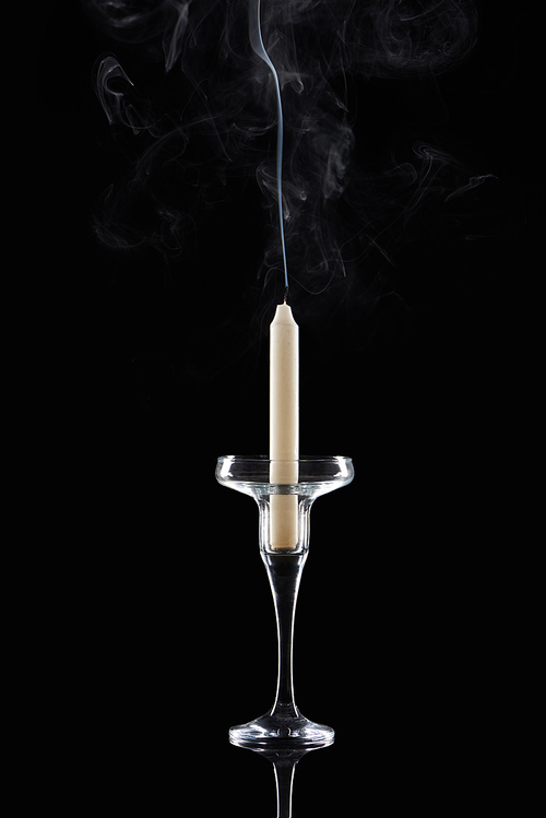 extinct white candle in glass candlestick with smoke on black background