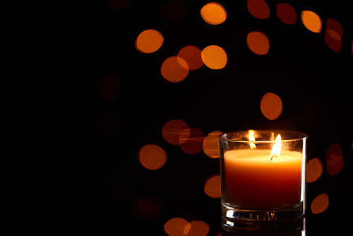 burning candle glowing in dark with bokeh lights on background