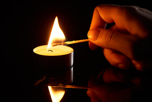 selective focus of woman lighting up candle with match isolated on black