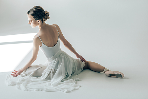 rear view of ballerina sitting in white dress and ballet shoes