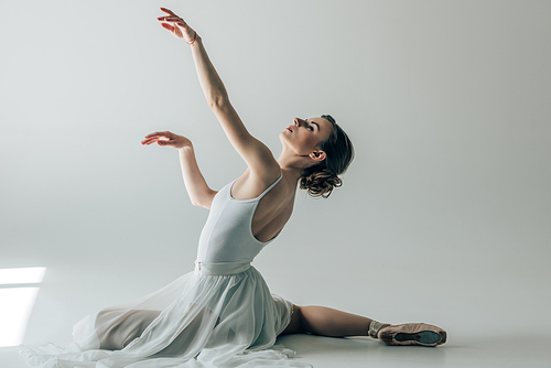 elegant ballerina sitting in white dress and ballet shoes